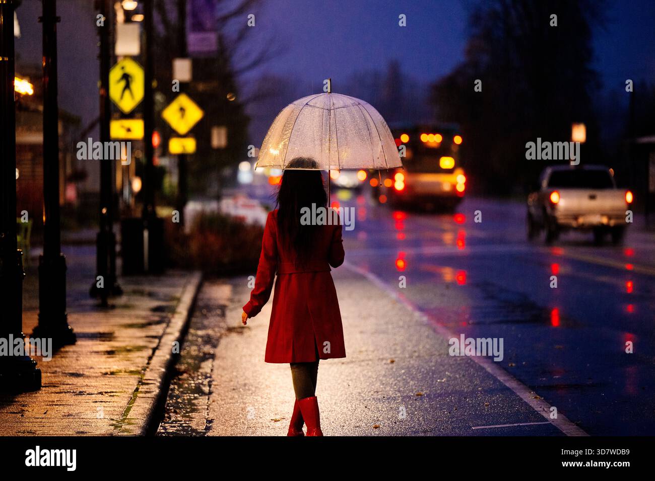 Woman in red coat walking at night with umbrella on a rainy city street ...