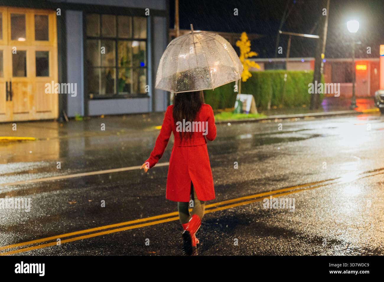 Woman in a red coat walking in the rain with a transparent umbrella at ...