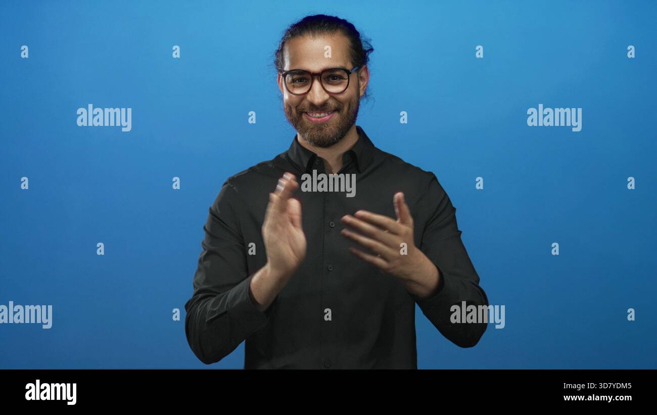 Man clapping hands and smiling in blue studio with glasses and beard ...