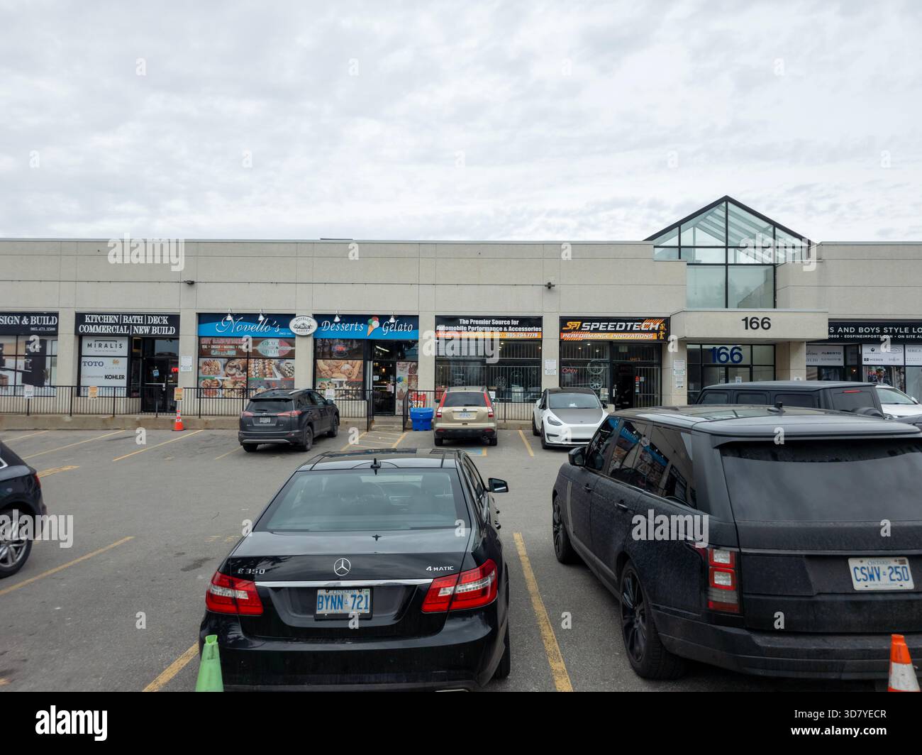 Commercial plaza with multiple auto service businesses, glass pyramid roof, parked cars, and cones. - Smartphone Captured Stock Image