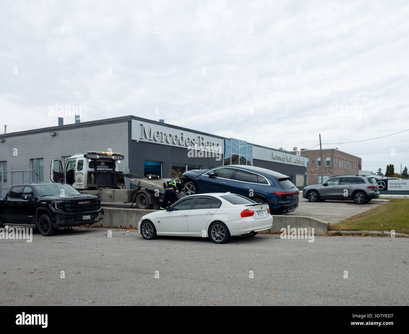 Mercedes-Benz dealership exterior with parked vehicles and SUV being loaded onto tow truck in Ontario. - Smartphone Captured Stock Image