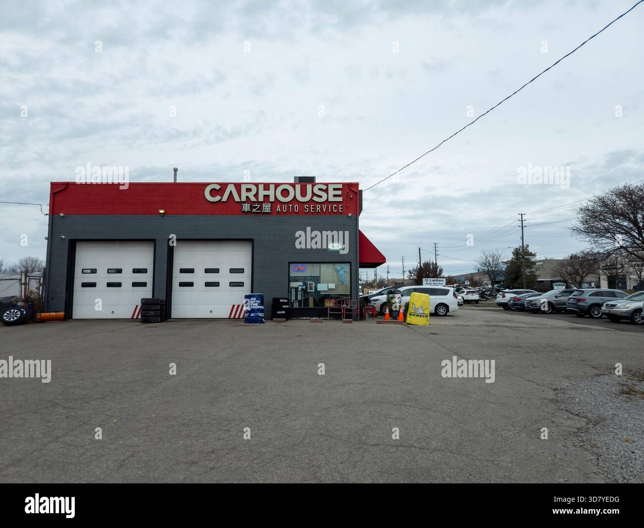 Carhouse D&M Auto Service building with red-gray exterior, garage bays, parked cars, and equipment. - Smartphone Captured Stock Image