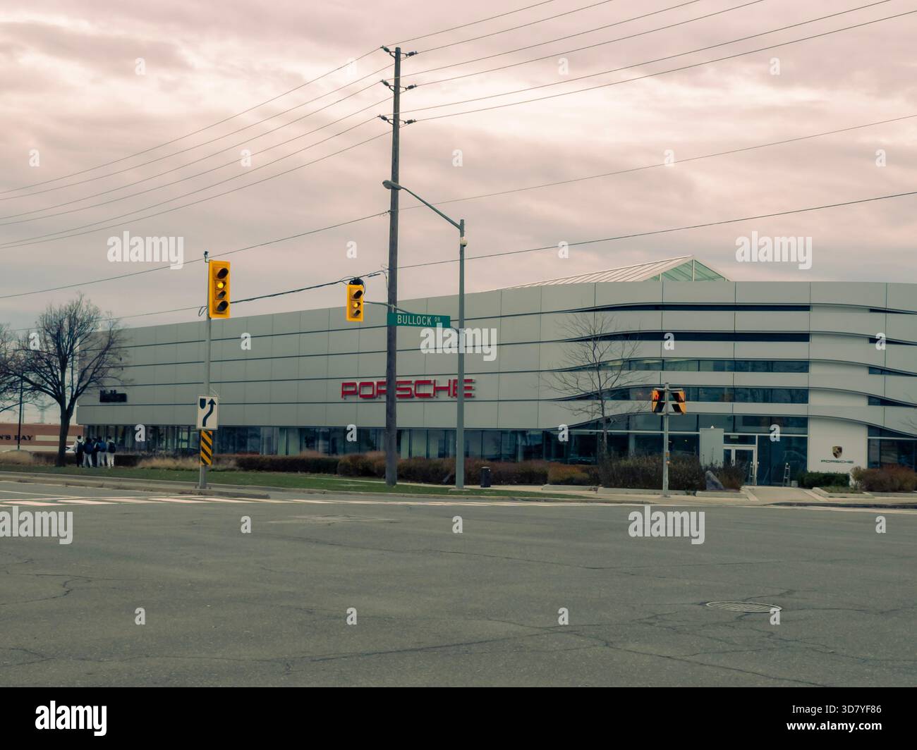 Porsche dealership at Bullock Drive with red logo, glass facade, traffic lights, and pedestrians. - Smartphone Captured Stock Image