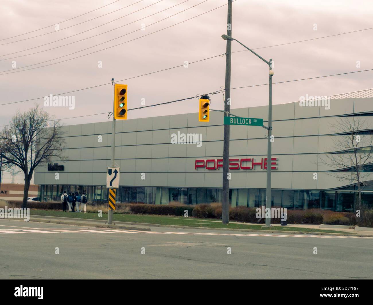 Porsche dealership at Bullock Drive with red logo, glass facade, traffic lights, and pedestrians. - Smartphone Captured Stock Image