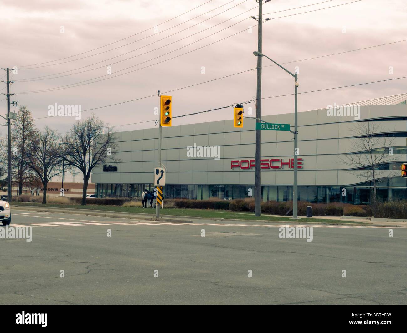 Porsche dealership at Bullock Drive with red logo, glass facade, traffic lights, and pedestrians. - Smartphone Captured Stock Image