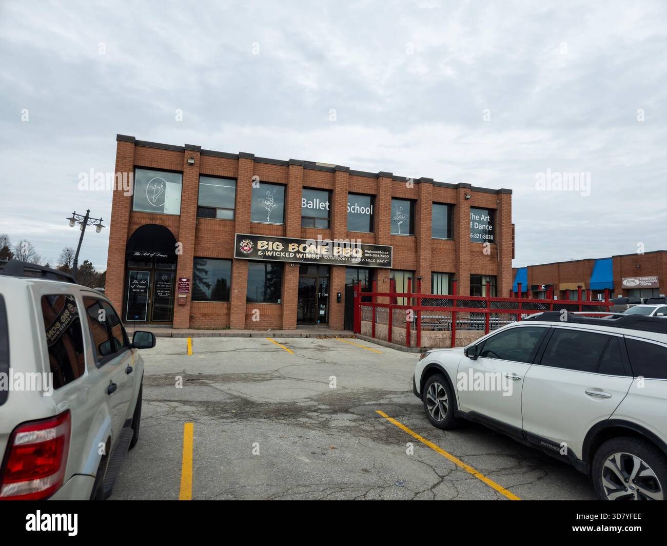 Two-story brick plaza with Big Bone BBQ, Ballet School, red railing, and parked cars in front. - Smartphone Captured Stock Image
