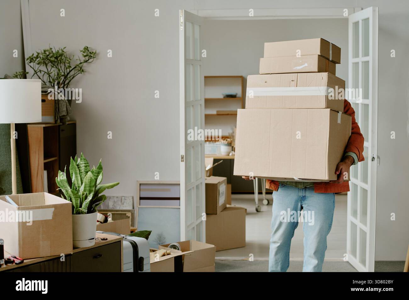 Young Man Carrying Cardboard Boxes While Moving into New Home Stock Photo