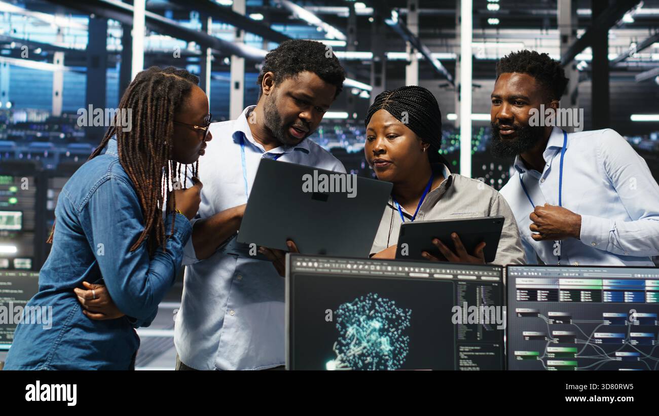 Portrait of smiling data center specialists collaborating in server facility, using node tree software to analyze datasets. Happy team using visual programming to improve gear performance, camera B Stock Photo