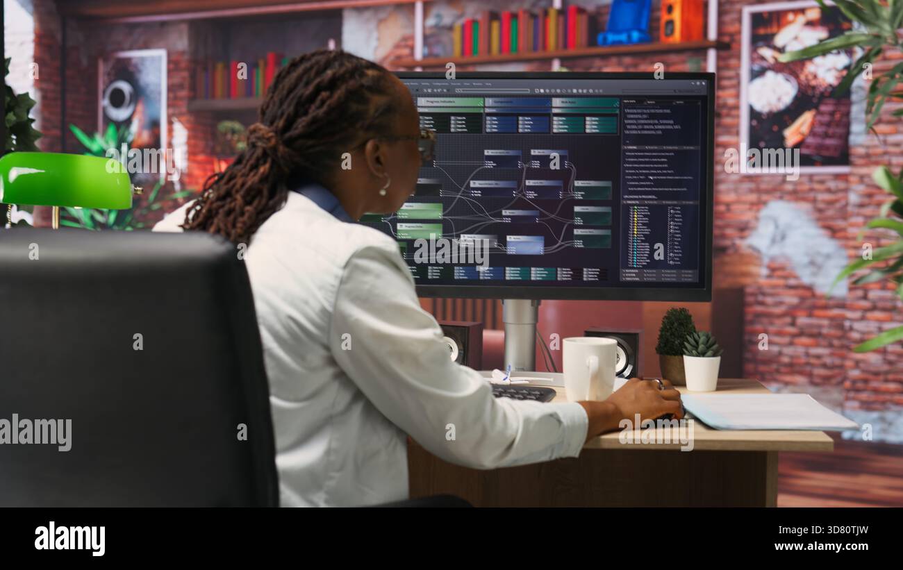 Teleworking computer scientist at home using PC to develop artificial intelligence self learning algorithms. African american woman working with AI machine learning software on PC, camera B Stock Photo