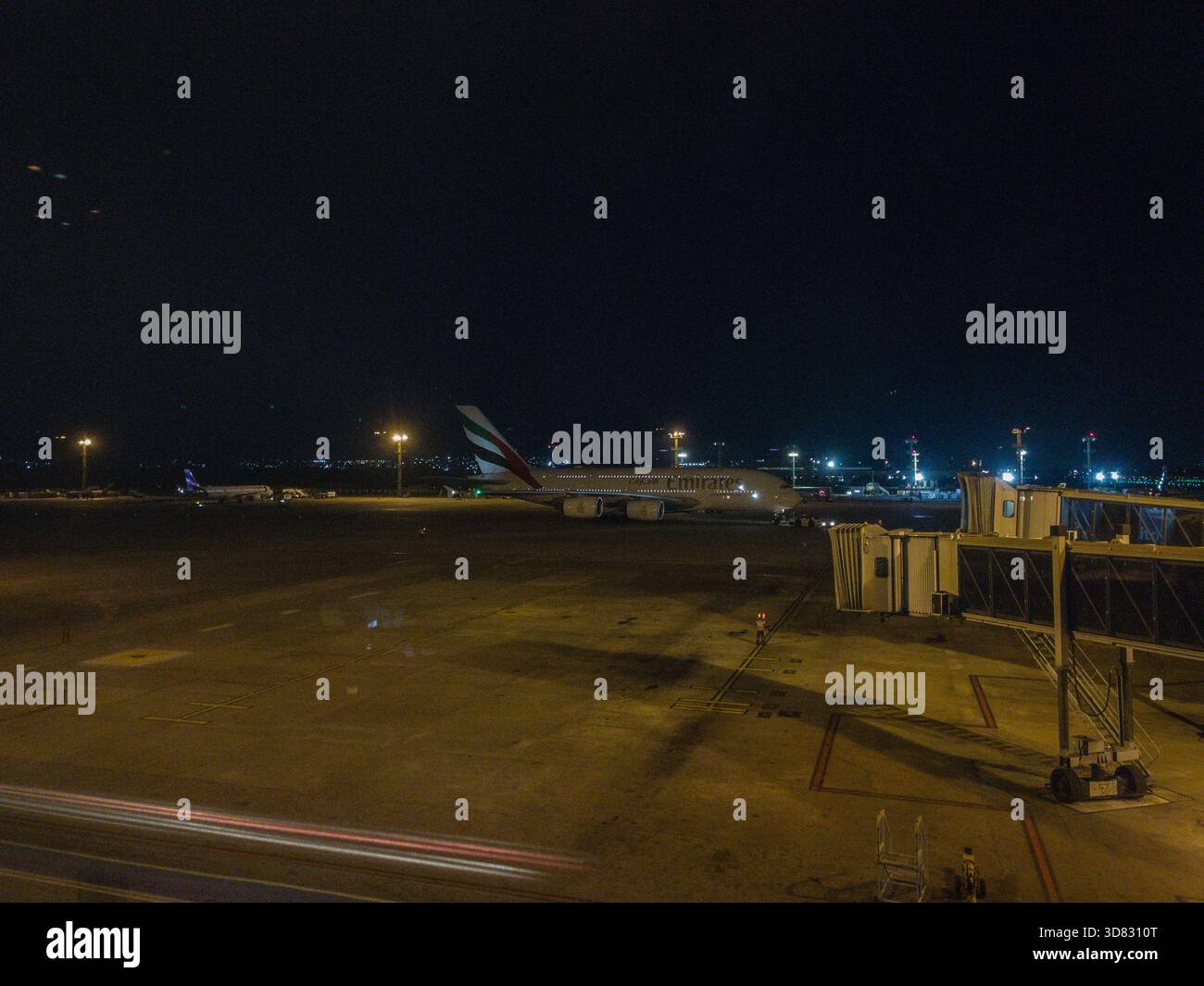 A view of Emirates Airbus A380-800 aircraft taxiing towards passenger boarding bridges at night at Dubai International Airport, United Arab Emirates - Smartphone Captured Stock Image