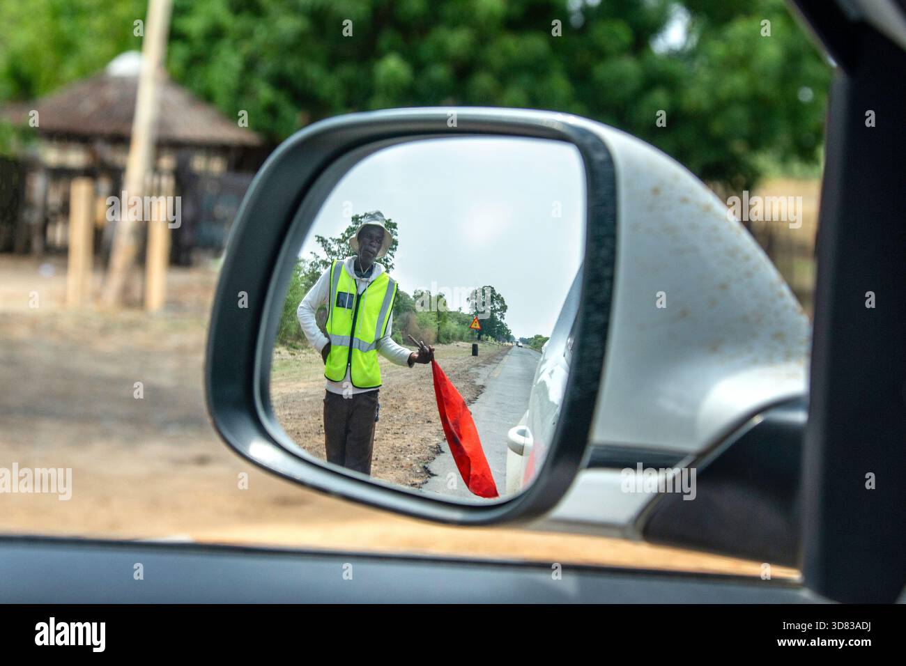 Road man controlling traffic with a red flag viewed through the car wing mirror. Stock Photo