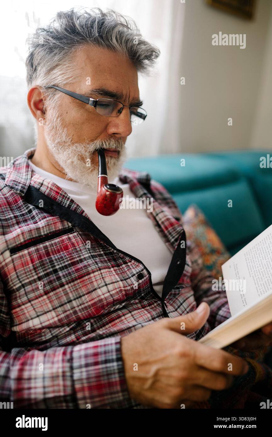 Older man reading a book while enjoying a pipe Stock Photo