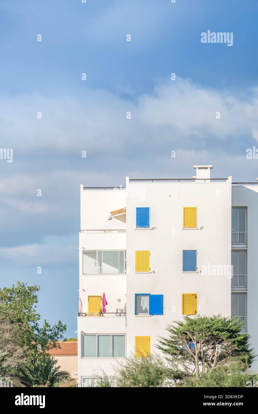 White modern apartment building facade with colorful yellow and blue shutters and balconies Stock Photo