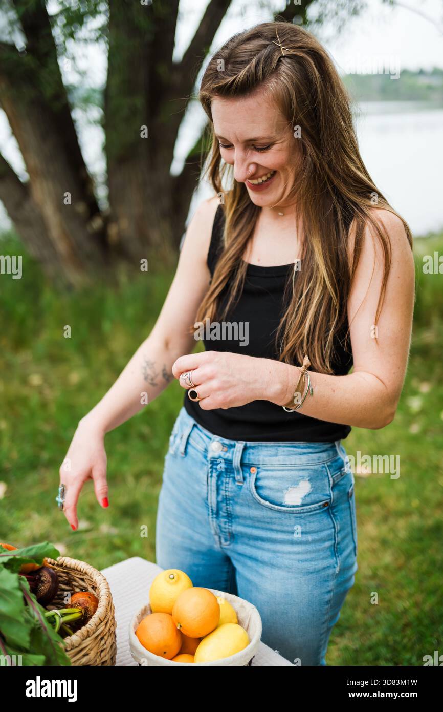 Smiling woman outdoors picking fruit from table baskets Stock Photo