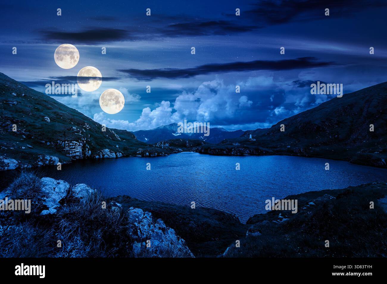 beautiful scenery with alpine lake at night. gorgeous clouds over the distant mountain ridge in full moon light. steep grassy slopes with rocks. backg Stock Photo