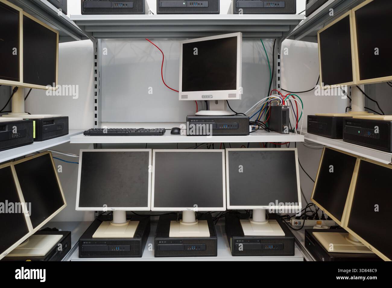 Multiple outdated desktop computers, including LCD monitors and horizontal processing units, arranged on white metal shelving. Stock Photo