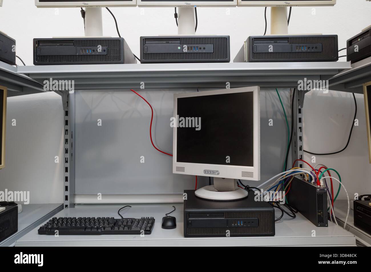 Multiple outdated desktop computers, including LCD monitors and horizontal processing units, arranged on white metal shelving. Stock Photo