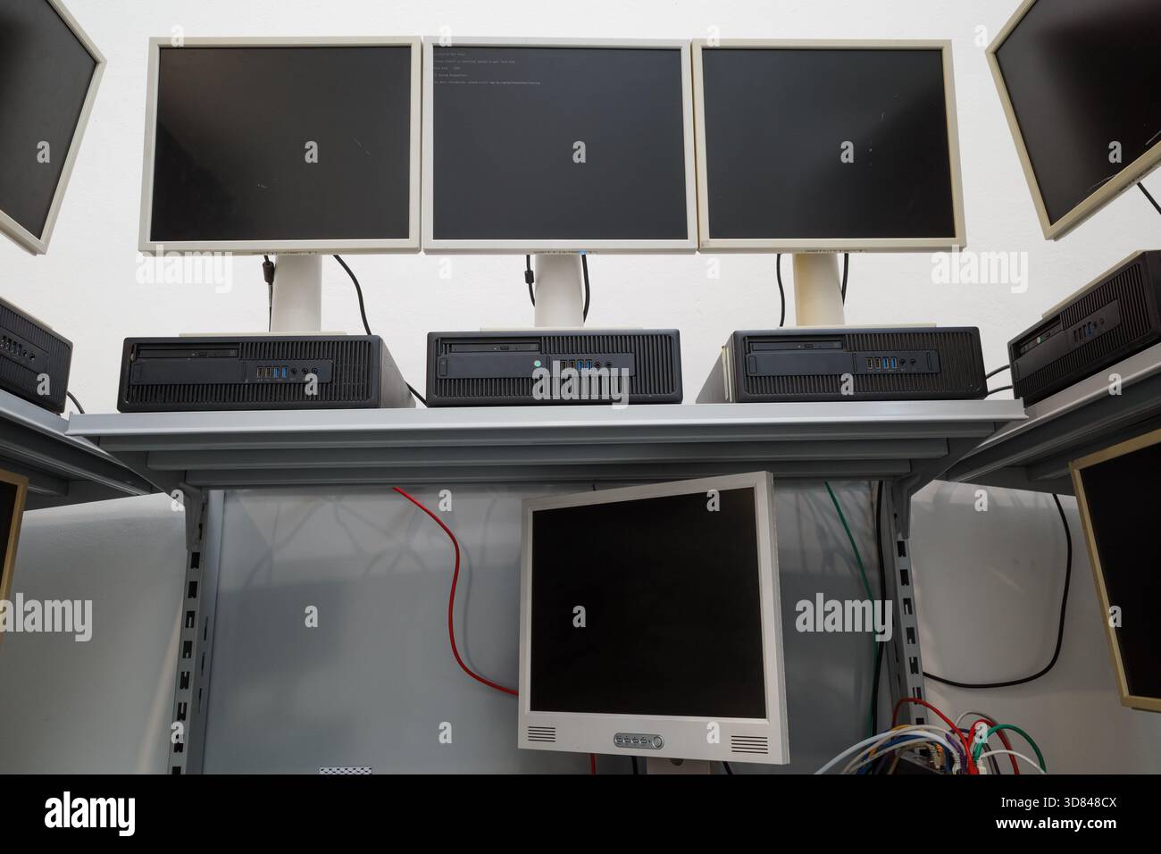Multiple outdated desktop computers, including LCD monitors and horizontal processing units, arranged on white metal shelving. Stock Photo
