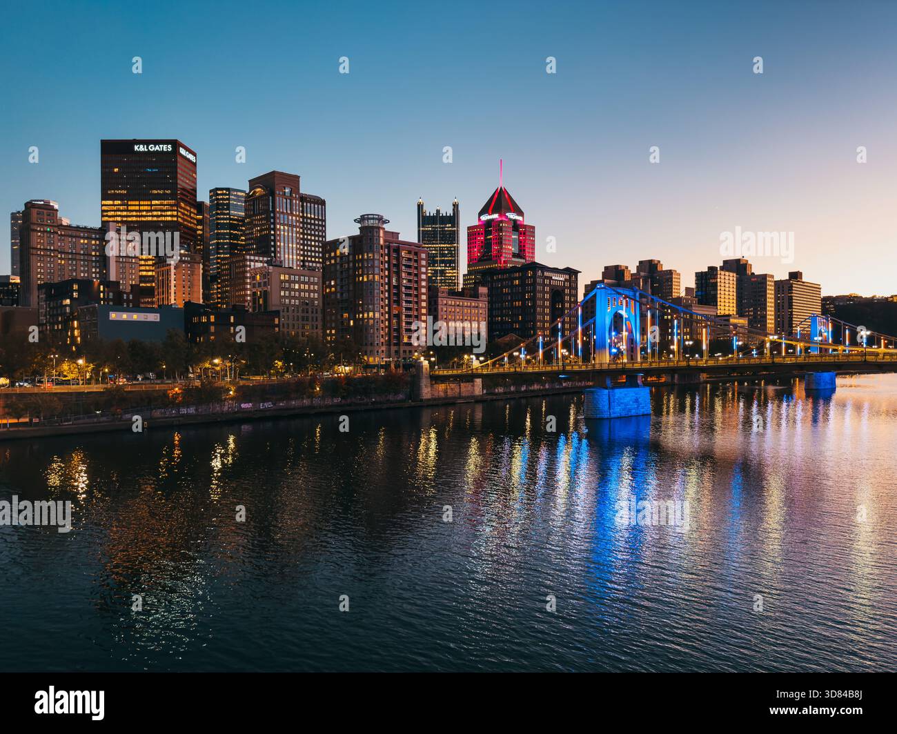 Pittsburgh skyline at dusk with illuminated skyscrapers and the blue-lit Roberto Clemente Bridge reflected in the Allegheny River. Stock Photo