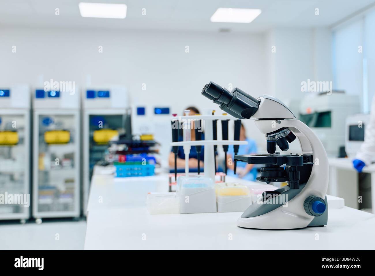 Microscope in a modern laboratory with scientists conducting research during daylight hours Stock Photo