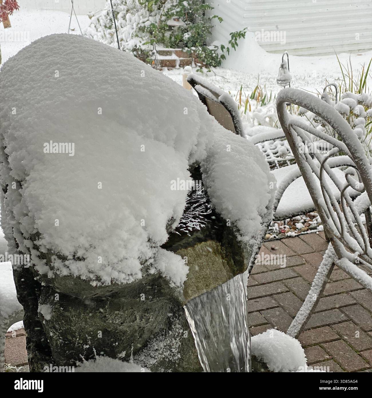 A backyard patio with a waterfall feature, patio chairs, and yard, covered in a layer of snow in Salem Lakes, Wisconsin, USA - Smartphone Captured Stock Image