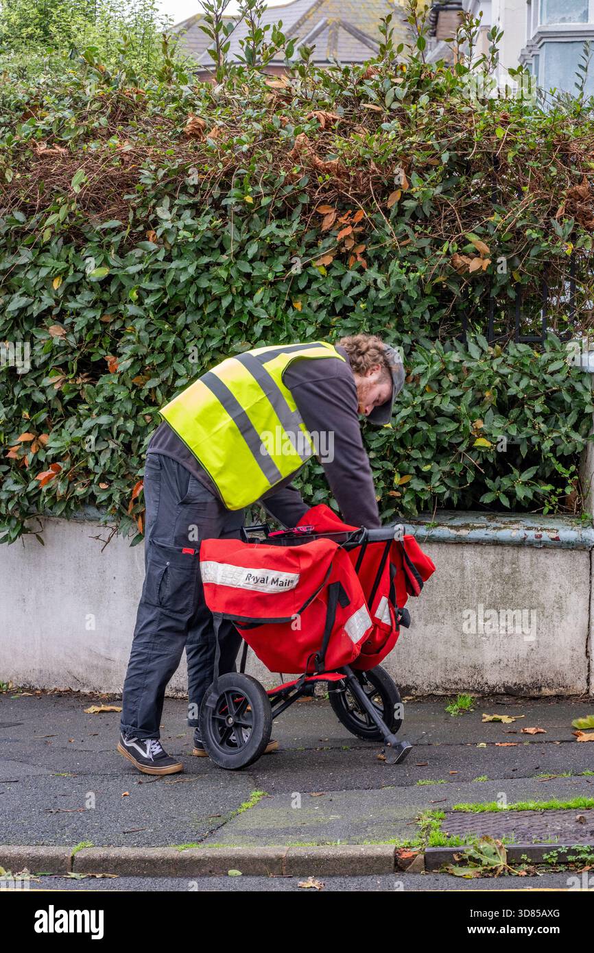 Postman on his rounds with small red trolley. Royal mail post office ...