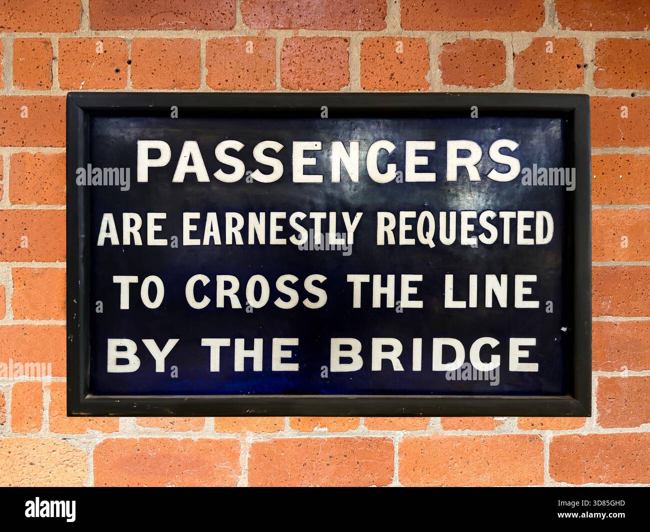 Vintage railway sign instructing passengers to cross the line using the bridge mounted on red brick wall - Smartphone Captured Stock Image