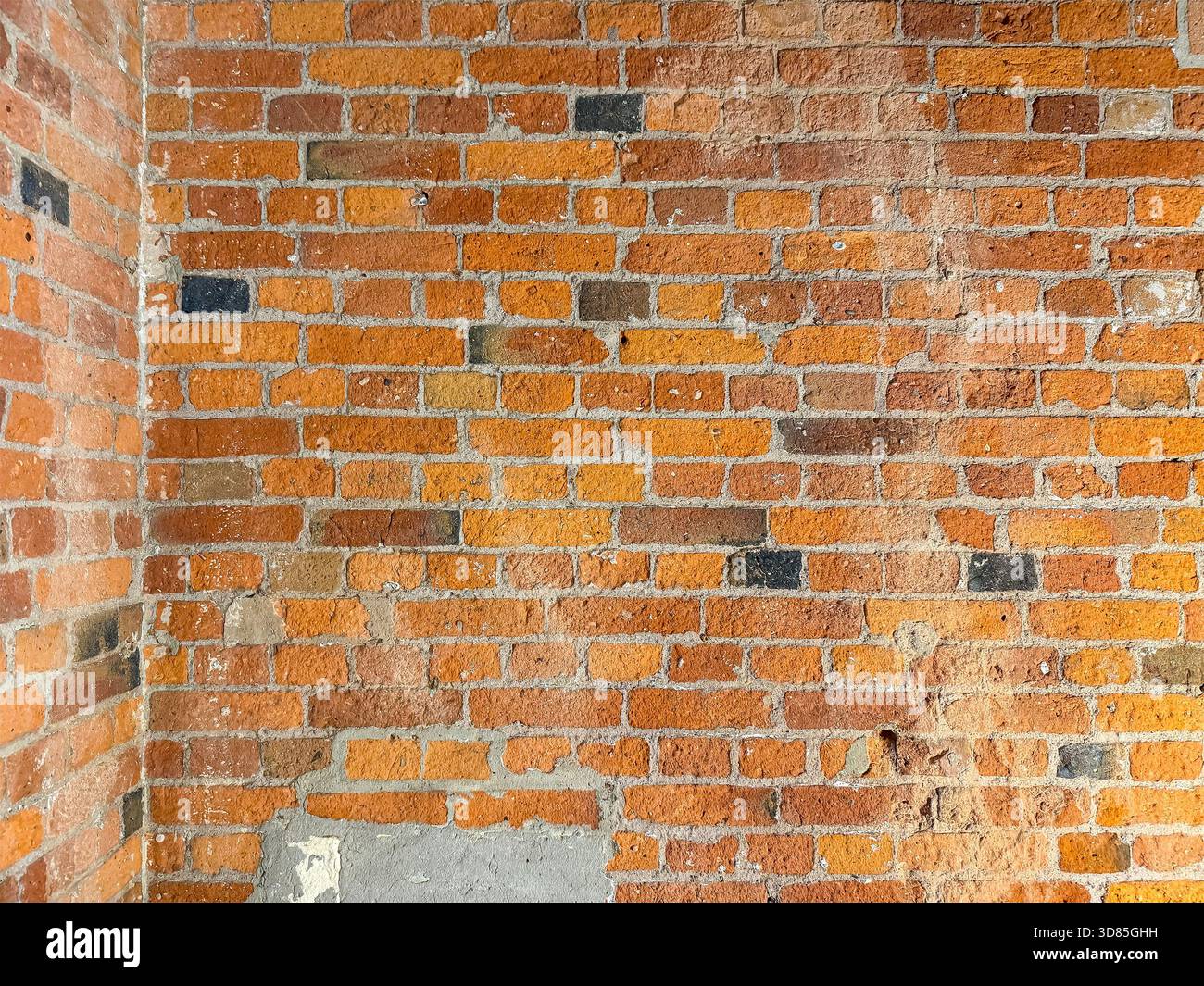 Old red brick wall with visible weathering, chipped paint and mortar variation in a corner interior or exterior surface Stock Photo