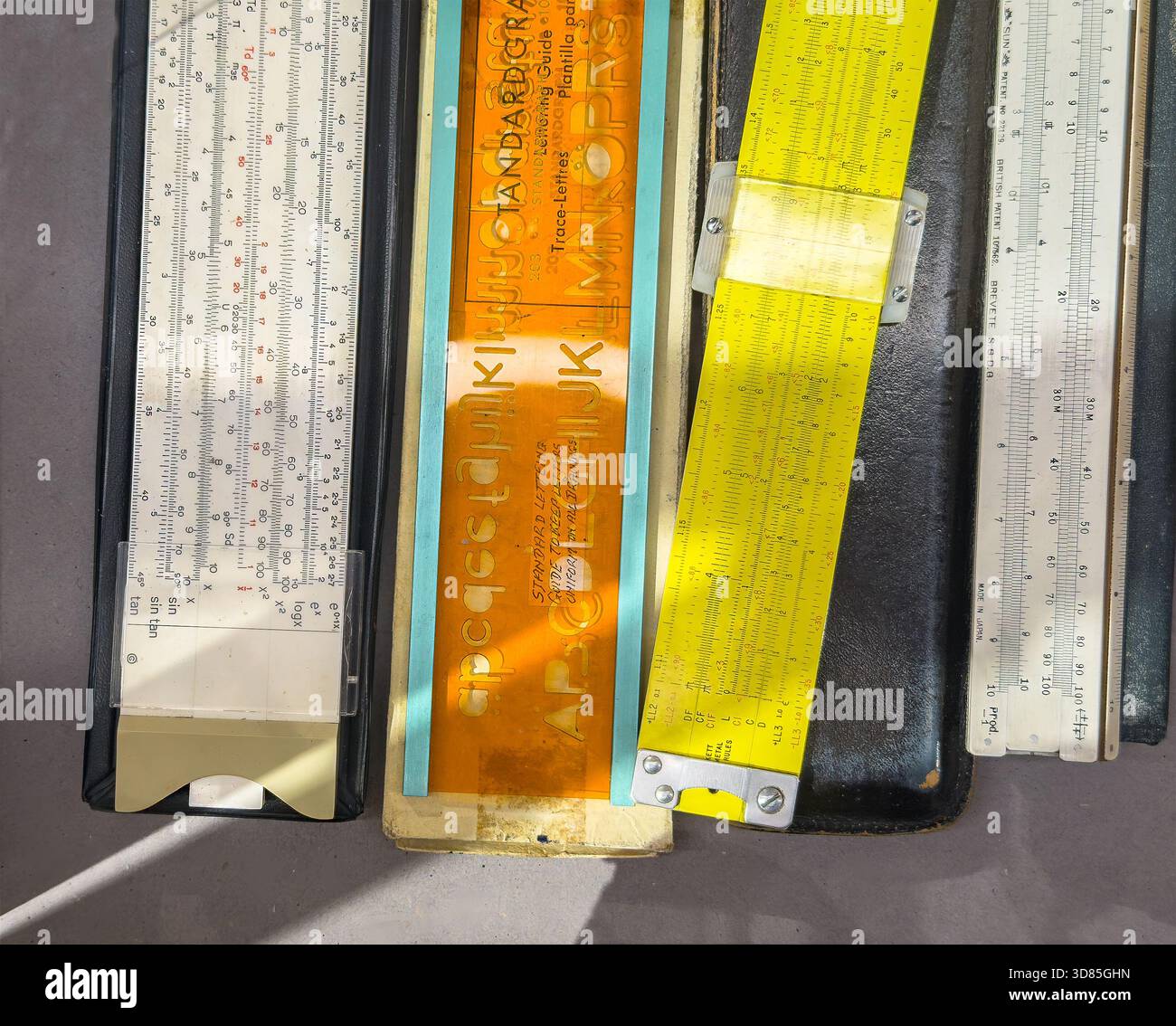 Collection of vintage slide rules and a lettering stencil template arranged on a table in direct sunlight - Smartphone Captured Stock Image