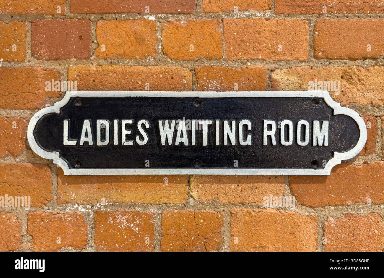 Vintage cast metal sign reading 'Ladies Waiting Room' mounted on a rustic red brick wall - Smartphone Captured Stock Image