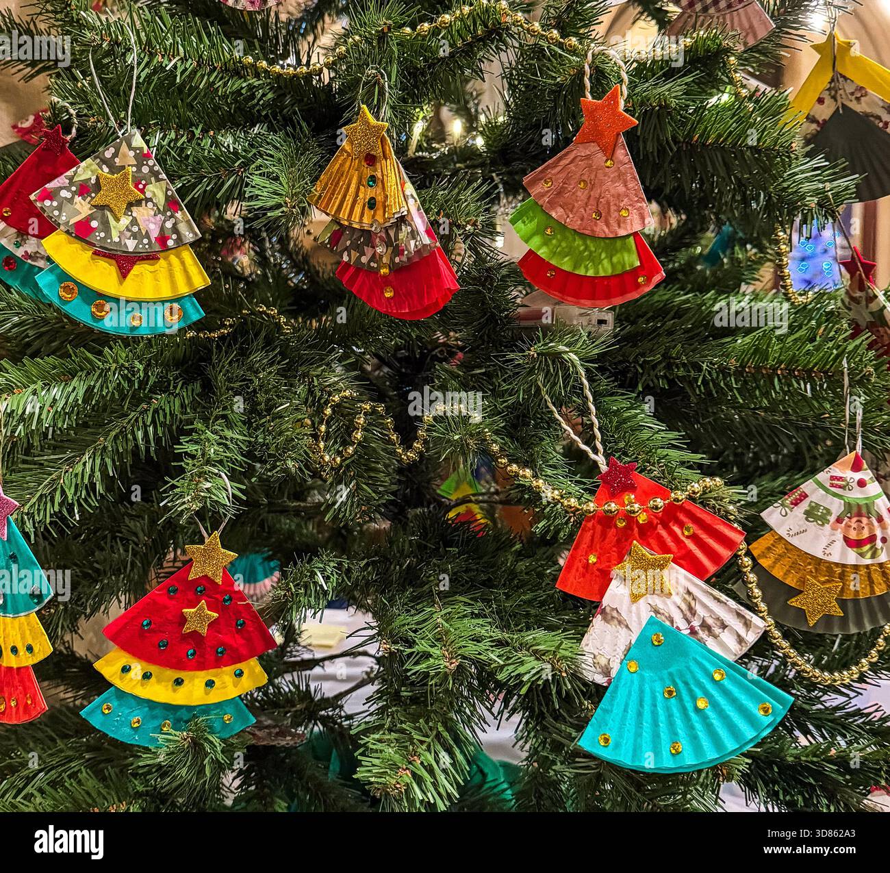 Colorful handmade paper Christmas tree ornaments hanging on a decorated green Christmas tree with festive lights St Mary's Church Calne - Smartphone Captured Stock Image