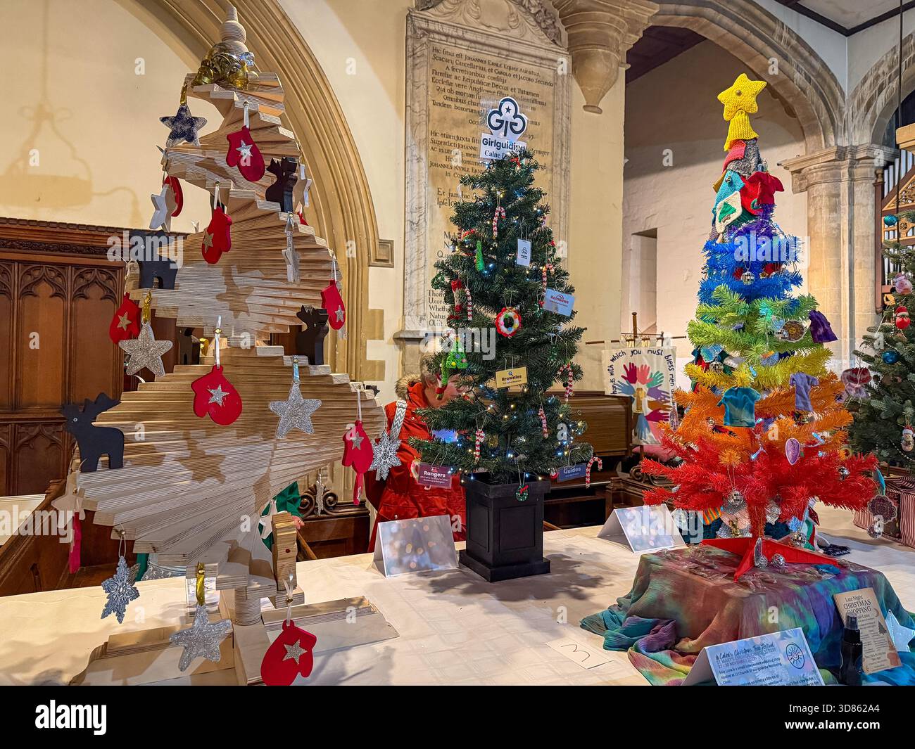 Colorful and creative Christmas trees on display inside a church with arched stone features  St Mary's Church Calne Christmas tree festival - Smartphone Captured Stock Image