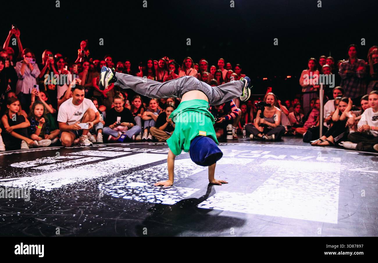 Breaking dancer in blue cap breaker handstand freeze circle, audience cheering under neon lights, victorious pose after round win Stock Photo