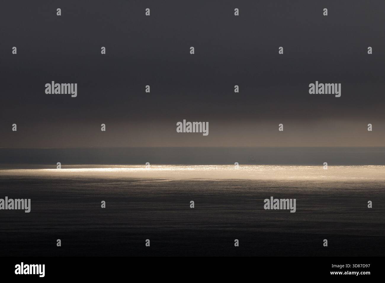 Sunlight breaking through clouds over dark ocean horizon Stock Photo