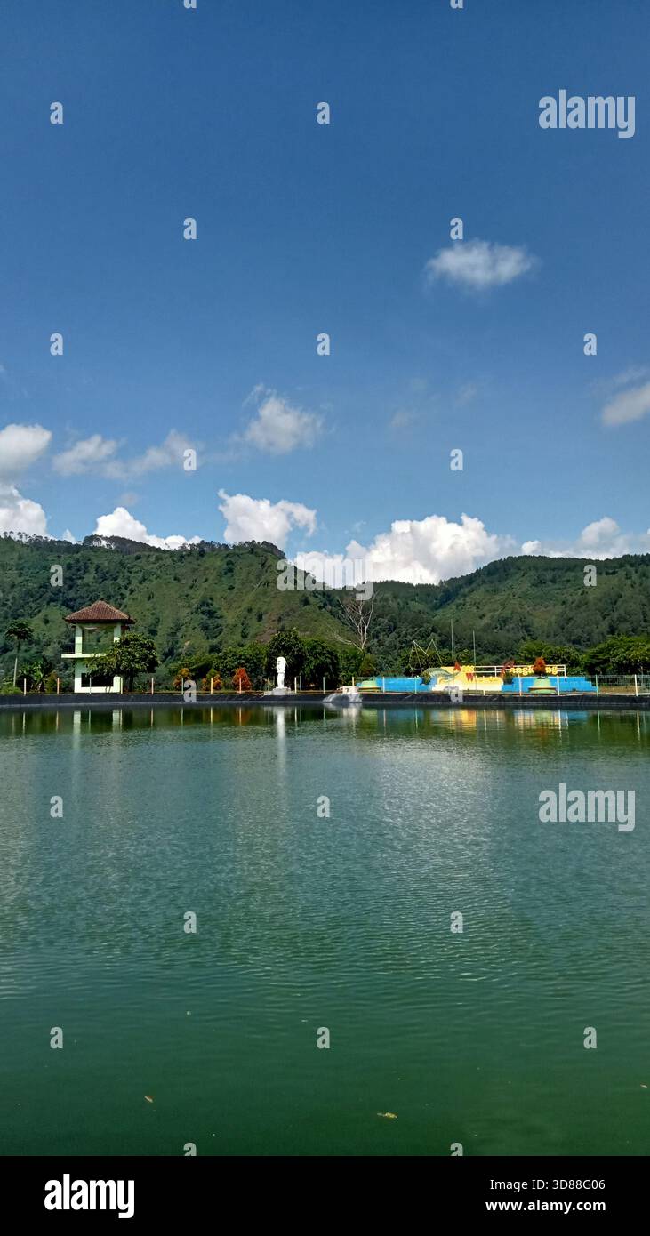 Scenic view of Embung Cangkring; a rainwater reservoir and tourism spot in Sadang, Kebumen, Central Java, Indonesia, with green hills and clear blue sky. - Smartphone Captured Stock Image