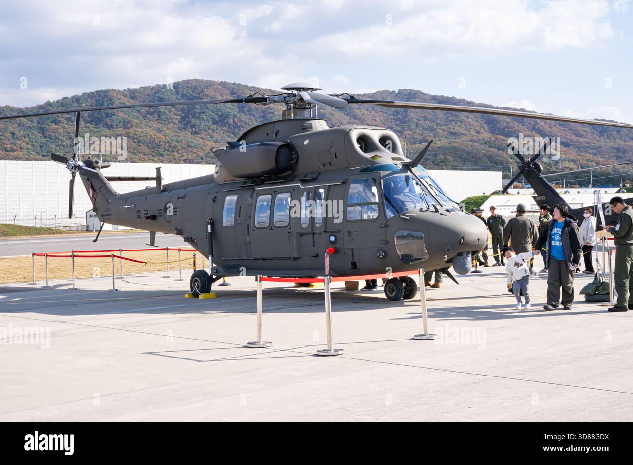 A military utility helicopter parked on an airfield with a crew member ...