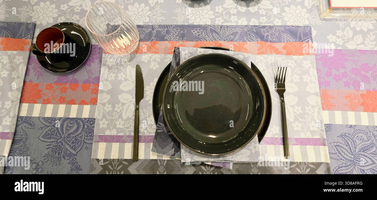 Berlin, Germany - September 19, 2025: Elegant table setting features black plates on colorful patterned linens with utensils. - Smartphone Captured Stock Image