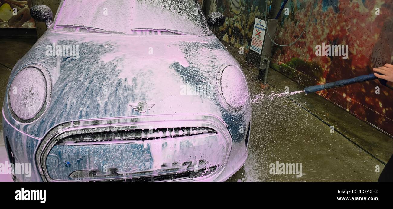 Berlin, Germany - May 18, 2025: Mini Cooper is being washed with foam in a colorful car wash environment. - Smartphone Captured Stock Image