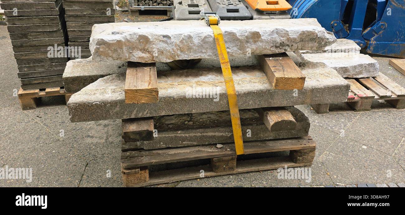 Berlin, Germany - September 22, 2025: Stacked stone blocks are secured with a yellow strap on wooden pallets in a construction area. - Smartphone Captured Stock Image