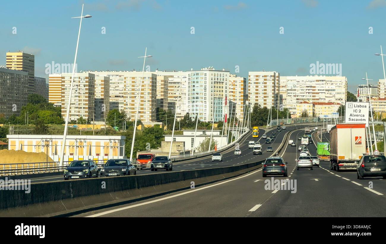 Lisbon, Portugal, May 20, 2025. A busy multilane highway curves toward high-rise residential buildings as vehicles pass beneath overhead cables marked Stock Photo