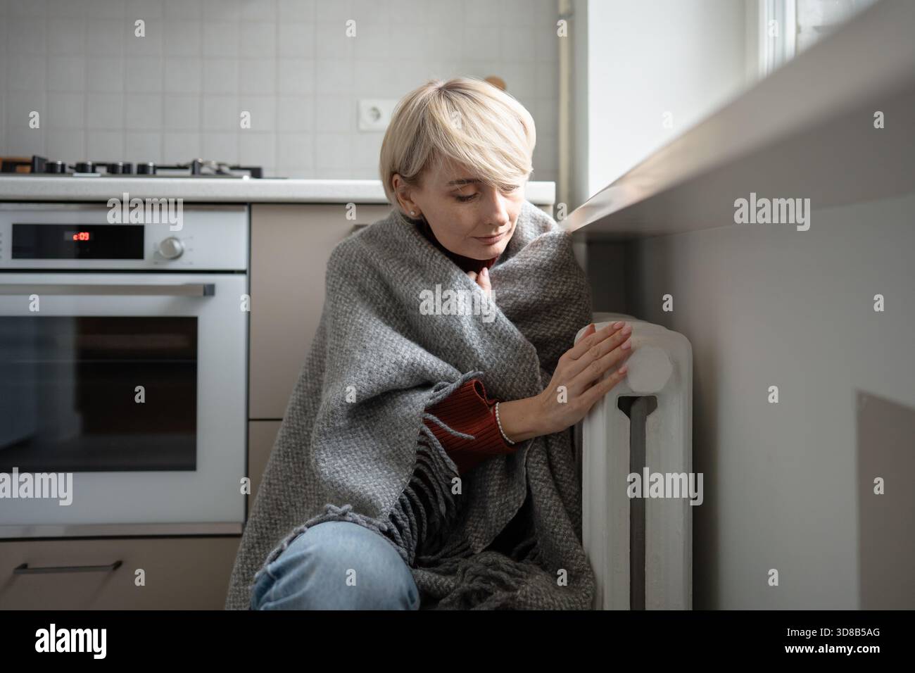 Woman warming hands on battery at home during winter. inadequate heating highlight, coldness indoor. Stock Photo