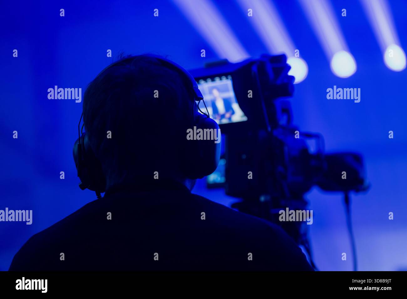 Silhouetted videographer operating a professional camera during a blue lit show with strong stage beams demonstrating modern media and event productio Stock Photo