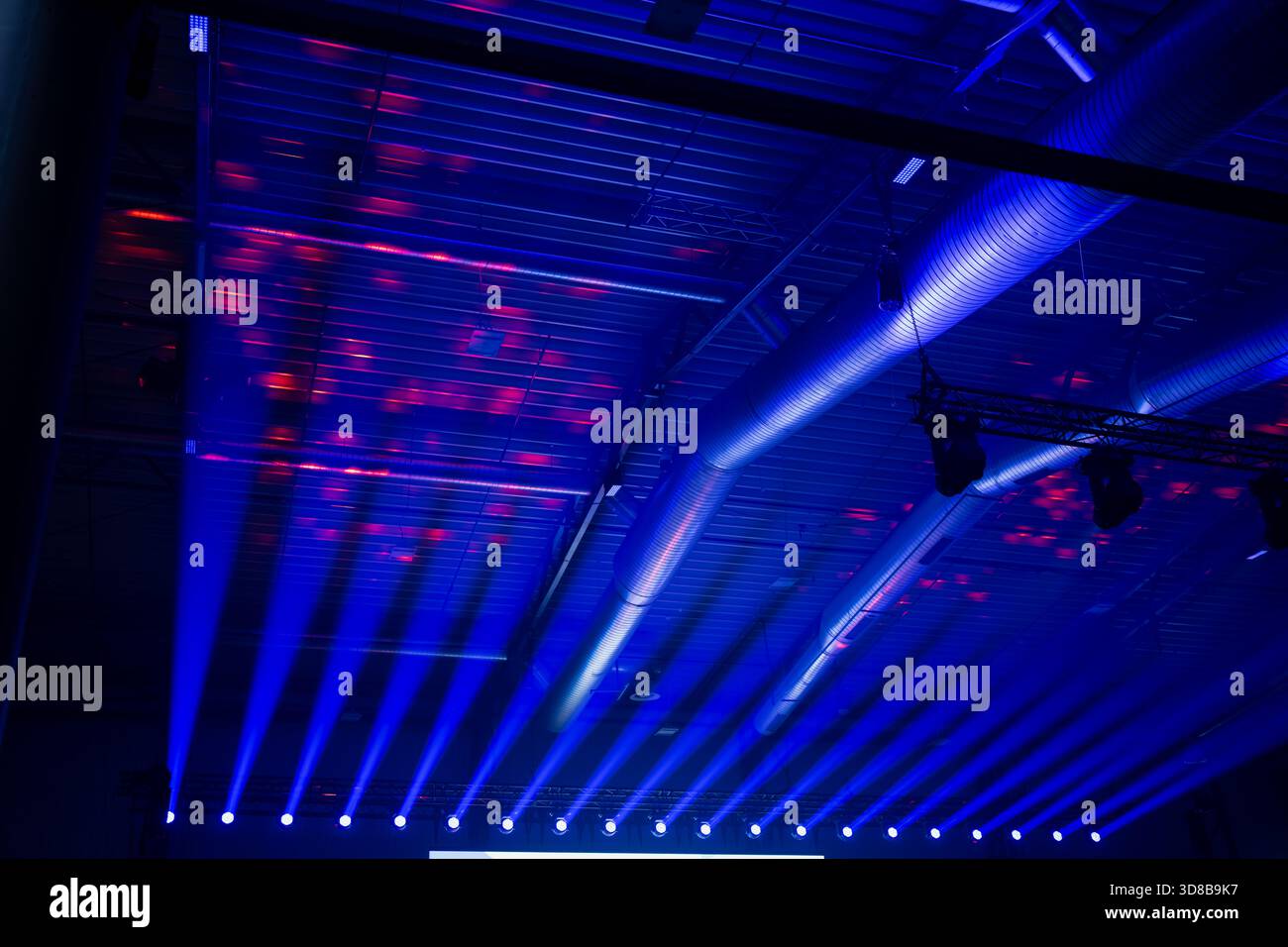 Strong blue stage wash beams projecting toward a metal ceiling with ...