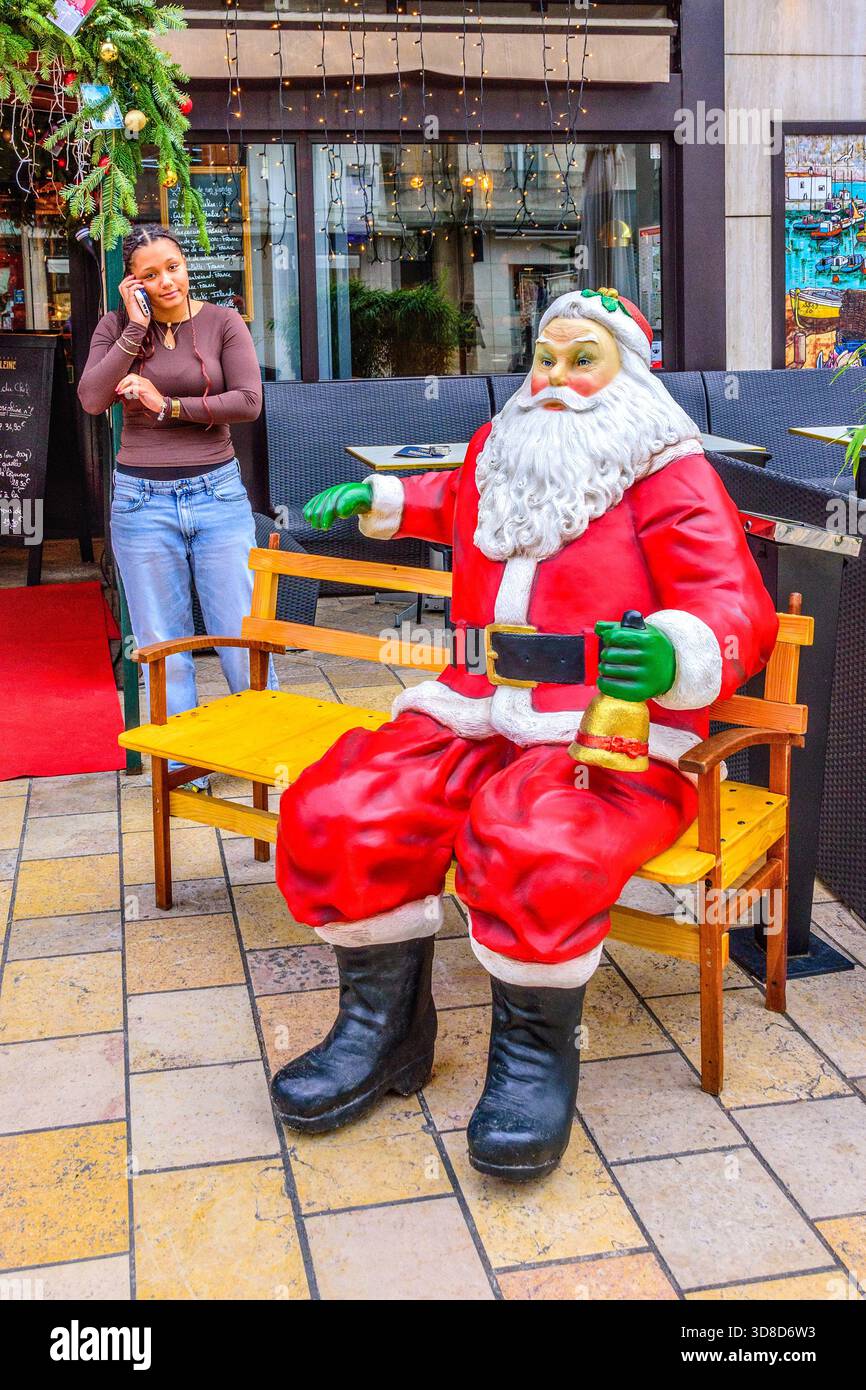 French-African woman on telephone next to a life-size Father Christmas display in city center - Tours, Indre-et-Loire (37), France. Stock Photo