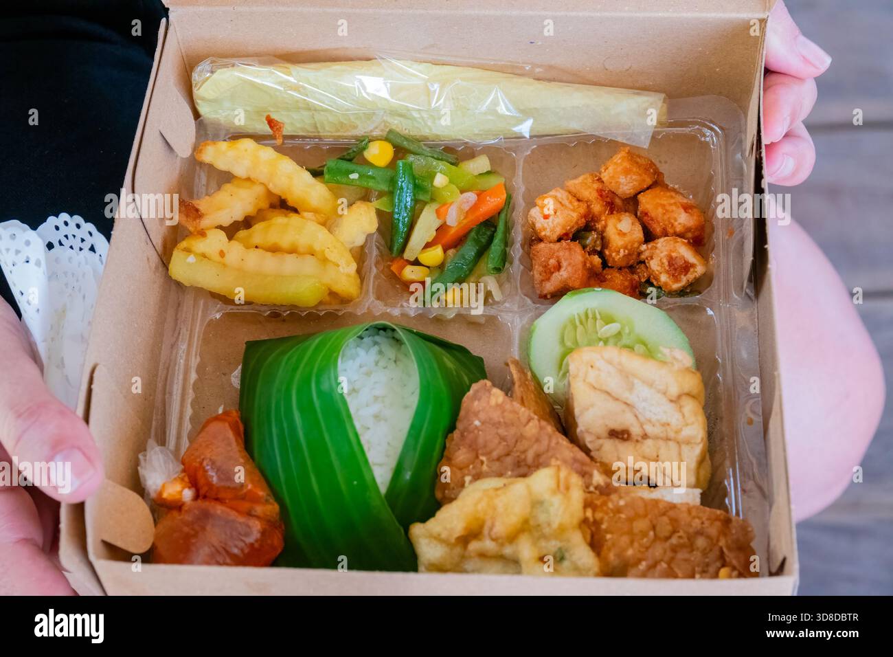 vegan lunch box, cardboard, tofu, tempeh, rice, french fries, vegetables, woman holding it, Komodo Island, Pulau Komodo, East Nusa Tenggara, Indonesia Stock Photo