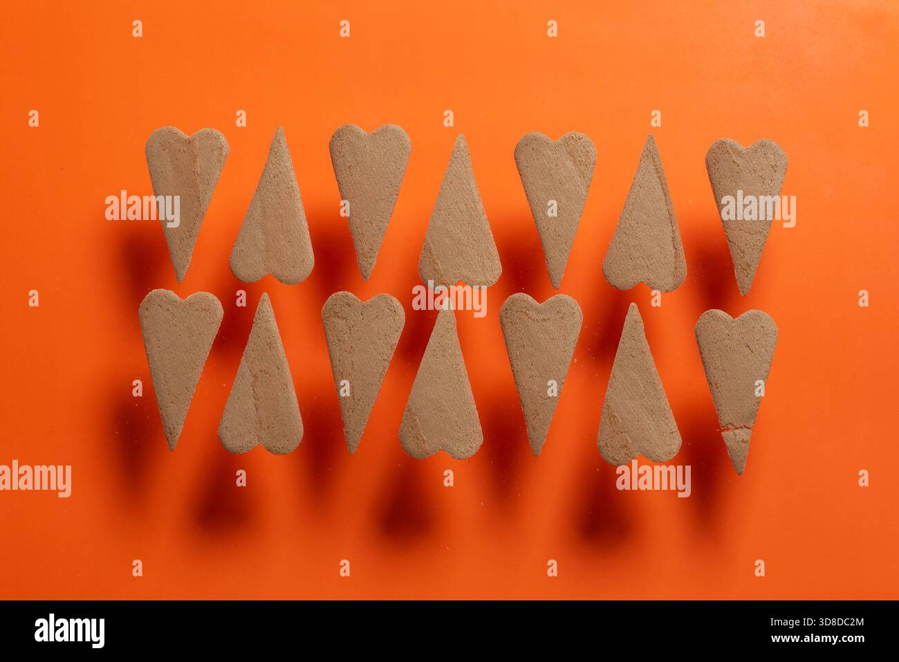 This image features heart-shaped sand forms arranged symmetrically on a vibrant orange background, creating a visually appealing abstract composition. Stock Photo