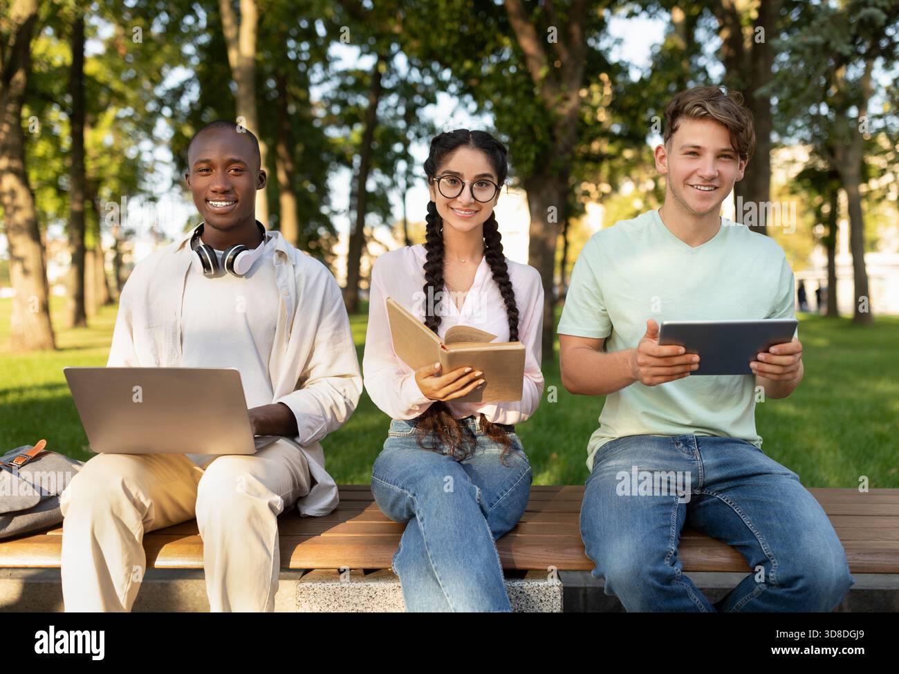 Students Work Together in a Park Using Laptops and Tablets During a Sunny Afternoon Stock Photo