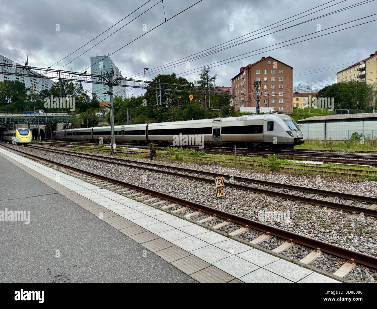 Trains passing through Solna Station in Stockholm, Sweden, on a cloudy day, with residential buildings and railway infrastructure in the background. - Smartphone Captured Stock Image
