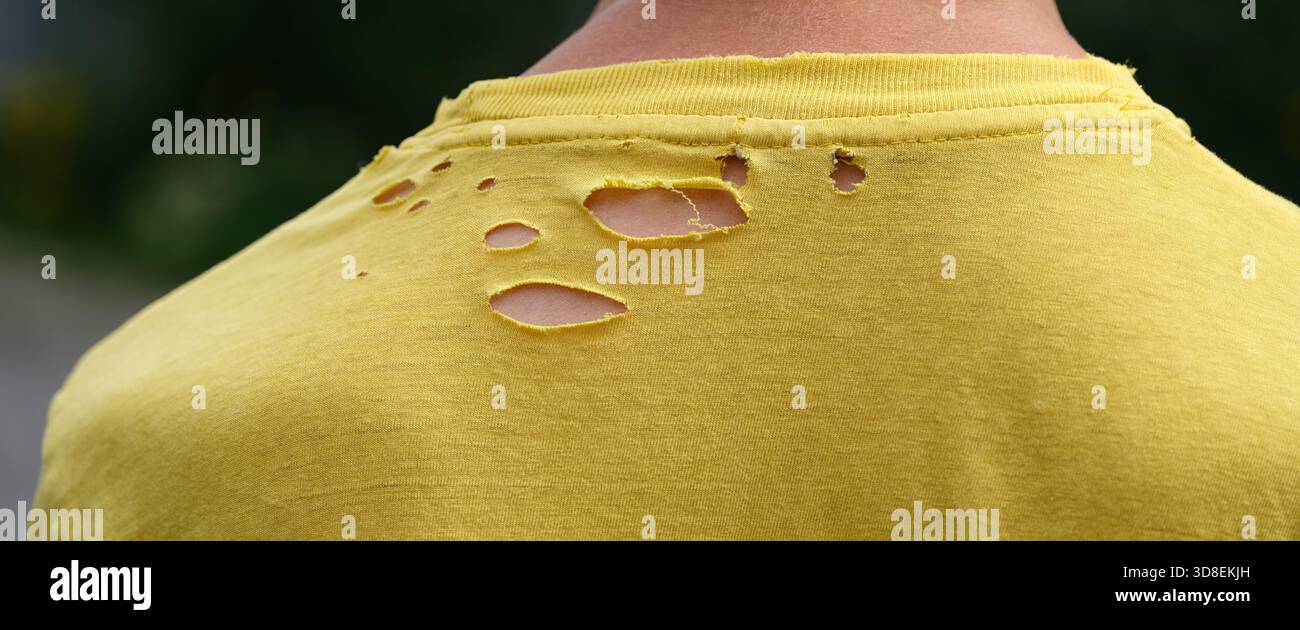 A close up shot of the back of a man wearing an old yellow t-shirt with holes in it. Close up. Stock Photo