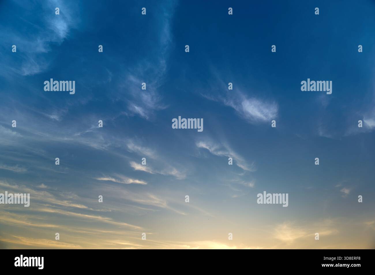 Deep Blue Sky with Wispy Clouds and Warm Evening Glow Stock Photo